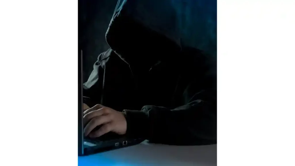 Hombre cubierto del rostro usando una laptop.
