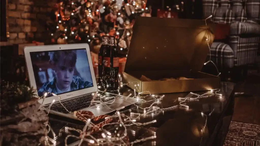 Mesa con luces navideñas, pizza, refrescos y una laptop con la película de Mi Pobre Ángelito.