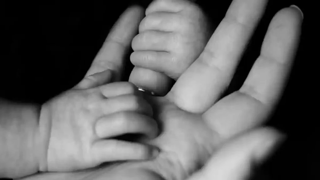 Foto en blanco y negro de la mano de un bebé sobre la mano de su madre.